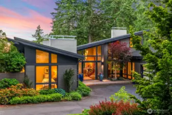 Modern yet welcoming, the home’s front façade balances clean geometry with rich natural textures. Mature landscaping and curated plantings lead to a glass-framed entry that hints at the design inspiration inside.