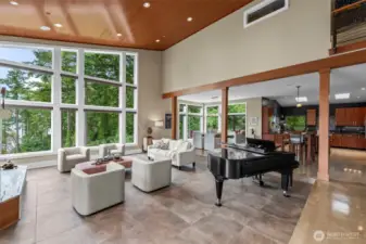 A dramatic gathering space filled with natural light, this great room captures the essence of modern Northwest living. Floor-to-ceiling windows frame serene views of evergreens and water, while the grand piano and open layout invite effortless entertaining.