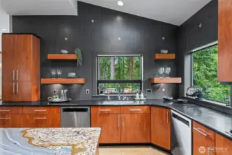 This architecturally striking kitchen is both a visual centerpiece and a culinary workspace. Bold tile, slab granite, floating shelves, and windows that frame the forest make this space feel grounded, sophisticated, and deeply connected to its natural surroundings.