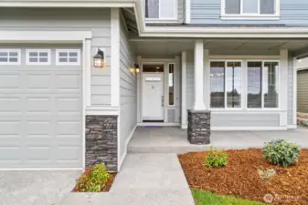 Covered front porch, accented by columns with stone bases, adds architectural charm and a cozy entryway.