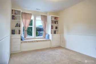 One of the two bedrooms at the front of the home with a window seat and cabinets, wainscoting on the walls.