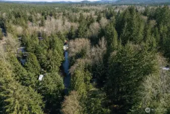 Aerial view showcasing the surrounding forested landscape and scenic waterway, offering privacy and natural beauty.