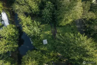 Top-down aerial highlighting the property layout with canal access, open lawn space, and surrounding mature trees.