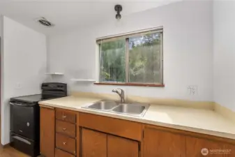 Enjoy wooded views and natural light from the kitchen window in this functional space featuring a classic double sink, fresh white walls, and open shelving. The newer appliances add value and efficiency—perfect for both first-time buyers and savvy investors.