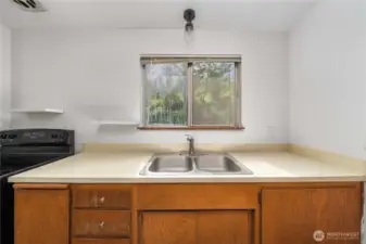 Enjoy peaceful views of the lush, tree-lined backyard while doing dishes at this centrally located double sink. Open shelving adds charm and practicality, while the natural light from the window keeps the space bright and airy.