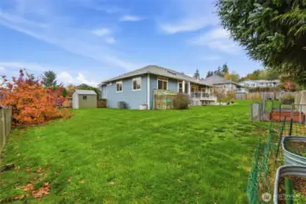 Fully fenced yard with greenhouse and deck for outdoor living.