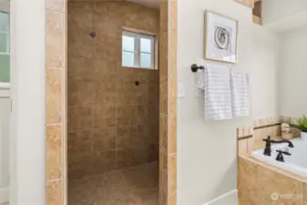 Large walk-in shower is surrounded by custom tile.