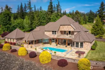 The west-facing side of the home features a slate-tiled pool deck, hot tub, covered seating area, and outdoor kitchen with gas fireplace