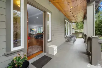 The covered front porch features a wood-planked ceiling, string lights, and enough room to sit and stay a while — with a direct view into the open main level.