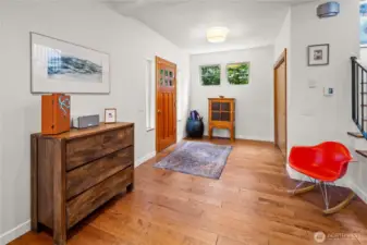 The main entry foyer is located on the mid-level of the home, accessed from a warm wood front door. Hardwood floors and a small window provide a welcoming arrival space. Stairs to the upper level are visible to one side.