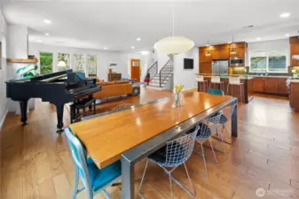The dining area sits at the heart of the open main floor, with a pendant light overhead and the kitchen's warm wood cabinetry, stainless appliances, and island visible in the background. The open flow between living, dining, and kitchen is clearly illustrated here.