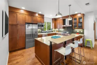 The kitchen is positioned adjacent to the dining area on the main floor. Warm wood cabinetry extends to the ceiling, housing built-in appliances, and the center island with composite countertop offers casual seating. Polished metal pendant lights hang overhead.