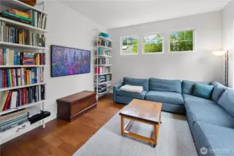 The den is located on the main living floor and features hardwood floors and a built-in floor-to-ceiling bookcase, creating a cozy atmosphere. Three horizontal windows bring in natural light while providing a sense of privacy. The space flows off the main living area as a dedicated retreat within the same level.