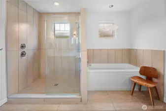 The shower and soaking tub area of the primary bathroom is clad floor-to-ceiling in large-format warm sand-tone tile. A glass-enclosed walk-in shower and a drop-in soaking tub occupies the other side.