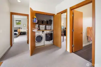 The upper level hall connects the bedrooms and keeps laundry convenient with a full-size washer and dryer tucked into a dedicated cabinet with shelving above.