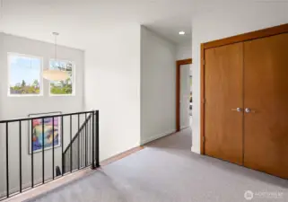The stair landing opens to the upper level with a saucer pendant, treetop views, and warm wood-trimmed doors leading to the bedrooms beyond.