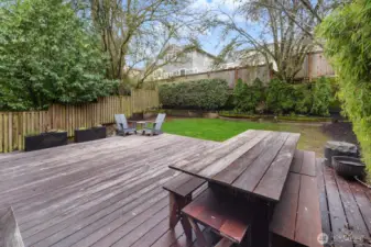 A spacious lower deck with room for dining and lounging opens to a fully fenced yard with raised planting beds, established hedging, and a generous lawn.