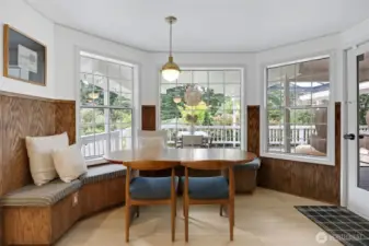 A warm and inviting eating nook with built-in seating, surrounded by windows that fill the space with natural light—complete with a door to the right for easy access to the covered deck.