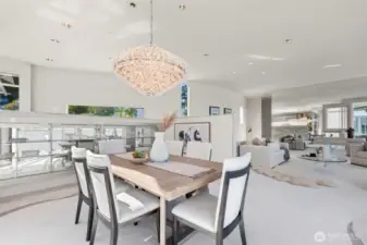 Positioned to capture both natural light and serene bay views, the dining space blends elegance with function. A sculptural crystal chandelier makes a statement overhead, while built-in glass display cabinetry adds a sleek, modern touch. Flowing seamlessly from the living room, this open-concept design is perfect for entertaining, offering a refined setting for intimate dinners or lively gatherings—all while showcasing the home’s distinctive waterfront architecture.