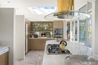 Gourmet kitchen with gas cooktop in marble island, sleek lucite cabinetry, and skylight that floods the space with natural light—perfect for cooking and entertaining in style.
