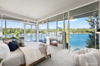 Jaw-dropping primary suite wrapped in floor-to-ceiling glass, offering panoramic waterfront views, a private balcony, and a double-sided fireplace for ultimate luxury and serenity
