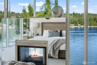 A see-through fireplace and walls of glass connect the primary suite to sweeping waterfront views, blending cozy warmth with an awe-inspiring natural backdrop.