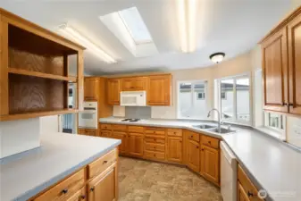 Warm wood cabinets and bright skylights give this modern kitchen an open, welcoming atmosphere, with natural light reflecting off clean countertops and white appliances.