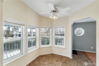 A window-wrapped breakfast nook filled with natural light, overlooking a gently flowing river. The warm, cozy space invites quiet mornings with coffee and a good book.