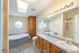 Light-filled primary bathroom with skylight, soaking tub, walk-in shower, and dual sinks.