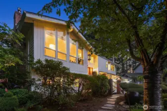 Architectural charm meets natural beauty! Expansive windows and warm evening light highlight the home’s mid-century design, surrounded by lush greenery and mature landscaping. The pathway and front entry create an inviting approach that blends seamlessly with the tranquil wooded setting. A perfect balance of elegance and Northwest character shines through every angle. ???