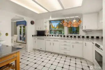 A cook’s dream featuring a wall of storage, sleek white appliances, and ample prep space. The checkered tile backsplash adds vintage charm, while the open layout connects effortlessly to the dining area for entertaining and everyday living.