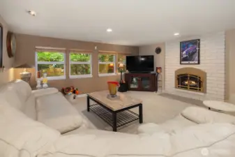 Spacious and inviting, this lower-level family room offers the perfect retreat for movie nights or casual gatherings. A wall of windows brings in lush garden views and natural light, while the cozy brick fireplace with elegant gold trim creates a warm focal point. The open layout easily accommodates a sectional and media setup—ideal for relaxation, entertaining, or creating a multi-use space. ????