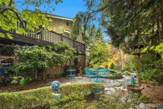 This beautifully curated garden features a koi pond framed by stonework and lush foliage. Multiple sitting areas and pathways connect seamlessly to the upper deck above.