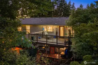 Twilight captures the warm glow of the home and its spacious upper deck surrounded by evergreens—perfect for entertaining or relaxing in your own woodland retreat. ???