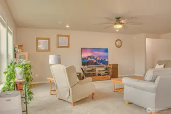 MAIN ROOM FROM DINING SPACE: Carpeted with Ceiling Fan, two South Facing Windows with 2" horizontal vinyl blinds, Shared Wall with Primary Suite; Hall to Primary Suite on Right (residence entry hall beyond frame to the right)
