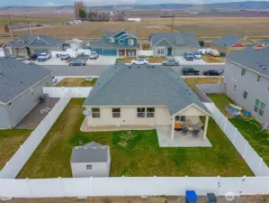 VIEW: North-Facing View of South-Facing Fully Fenced Backyard, Covered Patio with Roller Sunshades, Low-Maintenance Landscaping with In-Ground Sprinkler System, Storage Shed, and Alley Gate on Right Side of Frame