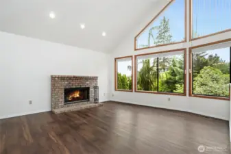 Living room with vaulted ceilings, abundance of natural light with wall of windows & wood burning fireplace.