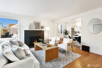 Sunny living room with wood-burning fireplace flows into the dining room.  Hardwood floors, freshly painted walls and large windows.