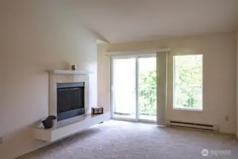 Living room with vaulted ceiling and cozy wood burning fireplace.  Slider to deck with storage.