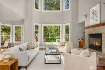 Dramatic two-story living room with fireplace, expansive windows, and serene garden outlook.