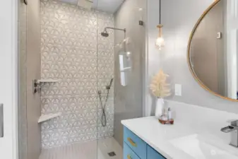 Elegant designer tiles grace the primary bedroom shower through a convenient walk-in glass surround. The custom vanity was crafted on-site with quartz counter, Kohler faucet and architectural lighting. Radiant heated floors make this bathroom especially cozy and relaxing.