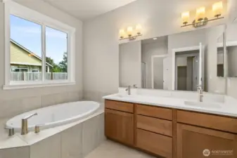 Primary bathroom has a double vanity with undermount dual sinks, tile floor, quartz countertops and a soaking tub with tile surround.