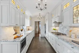 Carrera marble counter, lit custom cabinetry with leaded glass appliques, Liebherr refrigerator, Dacor gas stovetop and double ovens and Bosch dishwasher.