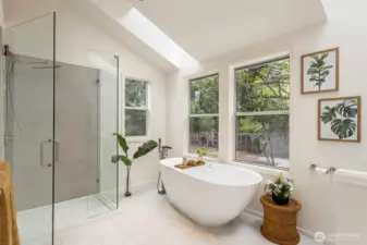 A spa-inspired bath with a freestanding soaking tub beneath a skylight invites you to unwind. Modern tilework, dual windows, and a glass walk-in shower elevate the experience.