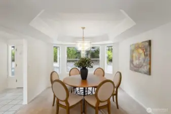 The dining area features a striking tray ceiling and surrounding windows that draw in natural light. A perfect setting for both intimate dinners and larger gatherings.