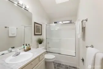 Bright and clean full bathroom featuring a skylight, tile countertop, and a tub/shower combo with sliding glass doors.