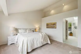 Spacious primary bedroom with vaulted ceilings, soft neutral tones, and an airy layout. Recessed lighting and natural light enhance the peaceful atmosphere.