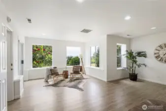 This lower-level living area is flooded with natural light from multiple large windows. Fresh flooring, garden & water views, and a modern layout make it ideal for gathering or relaxing.
