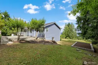 The side yard includes tiered patios and garden beds with space for outdoor dining, gathering, or planting.