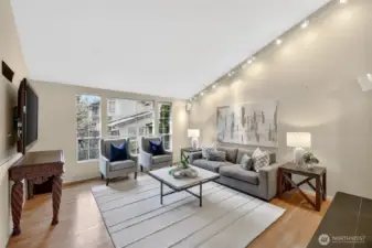 Bright living room with large windows, hardwood floors & stylish finishes. Spacious layout with cozy seating, modern lighting & great natural light. Gas firplace off to the right.
